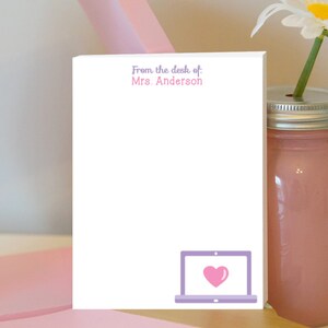 Op de afbeelding: Wit notitieblok met de tekst "From the desk of: Mrs. Anderson" bovenaan. Een paarse laptop met een roze hart op het scherm bevindt zich onderaan het notitieblok.