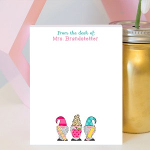 May include: White notepad with the text "From the desk of: Mrs. Brandstetter" at the top. Three gnomes are at the bottom of the notepad, one holding a ruler, one holding an apple, and one holding a pencil.