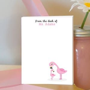 May include: A white notepad with the text "From the desk of: Ms. Adams" at the top. The notepad features a pink flamingo and a smaller pink flamingo chick.