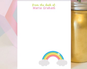 Può includere: Blocco note bianco con il testo "From the desk of: Maria Graham" in alto. Un arcobaleno con nuvole è in basso sul blocco note.