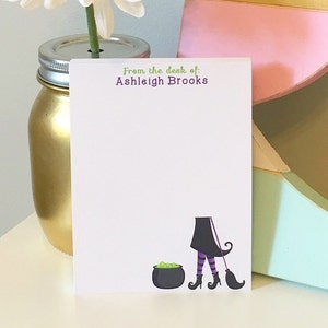 May include: A white notepad with the text "From the desk of: Ashleigh Brooks" at the top. The notepad has a cartoon illustration of a witch with a broom and a cauldron.
