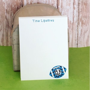 May include: White notepad with blue text that says "Tina Lipstreu". The notepad has a blue and black football with a white monogram "CLP" on it.