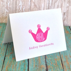 May include: A white card with a pink crown and the initials "AHL" inside. The text "Audrey Hershkovitz" is printed below the crown.