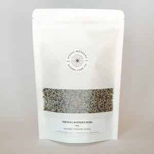 May include: A white pouch containing dried French lavender buds. The pouch has a clear window displaying the lavender. The label states "French Lavender Buds" and "50 g". The Works Wonders Herbal Care Co. logo is visible.