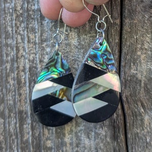 May include: A pair of teardrop-shaped earrings with black and white geometric patterns and iridescent abalone shell accents.
