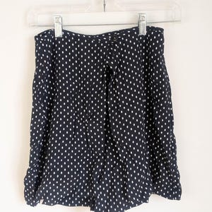 May include: Navy blue shorts with a white polka dot pattern, hanging on a clear hanger. The shorts have a high waist and a loose fit. The fabric appears to be lightweight.