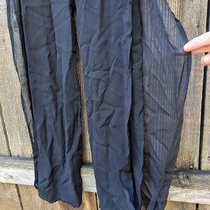 Puede incluir: Pantalones palazzo negros transparentes con perneras anchas. Los pantalones están hechos de una tela ligera y fluida. Los pantalones tienen cintura alta y un ajuste relajado. La tela es ligeramente transparente.