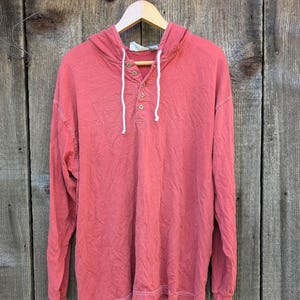 May include: A long-sleeved, coral-colored hooded shirt with a button-up front and white drawstrings. The shirt has a relaxed fit and is made of a soft, comfortable fabric.