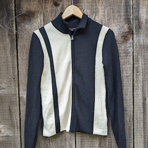 Puede incluir: Suéter a rayas blancas y negras con cierre de cremallera. El suéter tiene cuello alto y mangas largas.