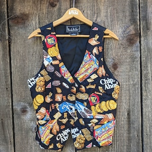 May include: Black vest with a pattern of various snack food items, including cookies, crackers, and peanuts. The vest features a V-neck design and a button closure. The words "Chips Ahoy!" and "Ritz" are visible on the vest.