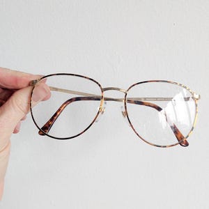 May include: Gold-rimmed eyeglasses with a tortoiseshell pattern on the temples. The glasses have a round shape and clear lenses. The text "REGIONAL OFFICE + 17" is visible on the frame.