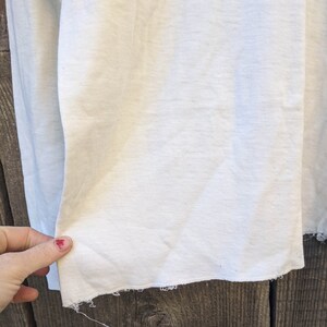May include: Close-up of a white fabric with a raw edge. The fabric is smooth and has a slight sheen.