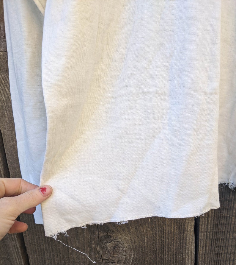 May include: Close-up of a white fabric with a raw edge. The fabric is smooth and has a slight sheen.