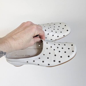 May include: White leather slip-on shoes with star-shaped cutouts. The shoes have a rounded toe and a low heel. The brand name "beauty fish" is visible inside one shoe. The shoes are shown against a white background.