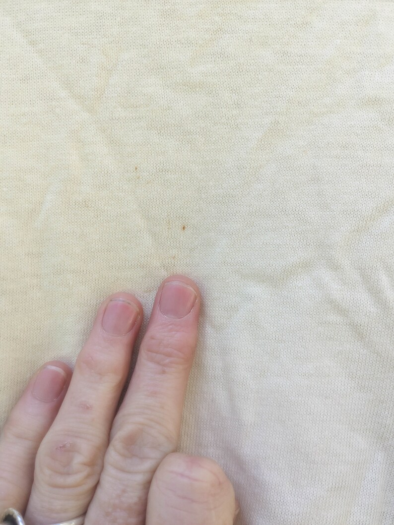 May include: Close-up of a light beige fabric with a few small brown stains.