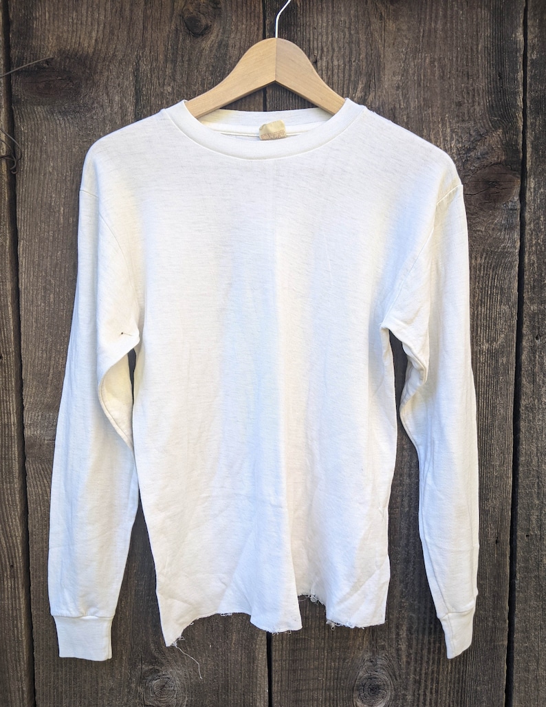 May include: A white long-sleeved t-shirt with a distressed hem and a small tag on the collar.