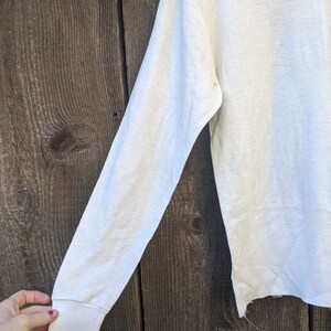 May include: White long-sleeved shirt with a slightly frayed hem. The shirt is made of a soft, lightweight fabric.