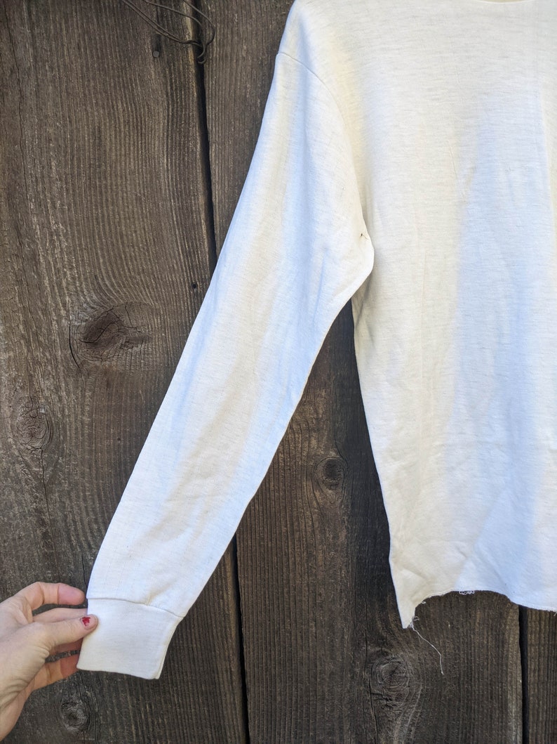 May include: White long-sleeved shirt with a slightly frayed hem. The shirt is made of a soft, lightweight fabric.