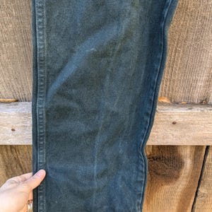 May include: Close-up of the dark green fabric of a pair of trousers. The fabric has a subtle texture and a slight sheen.