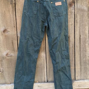 May include: A pair of dark green denim jeans with a leather patch on the back pocket that says "Wrangler".