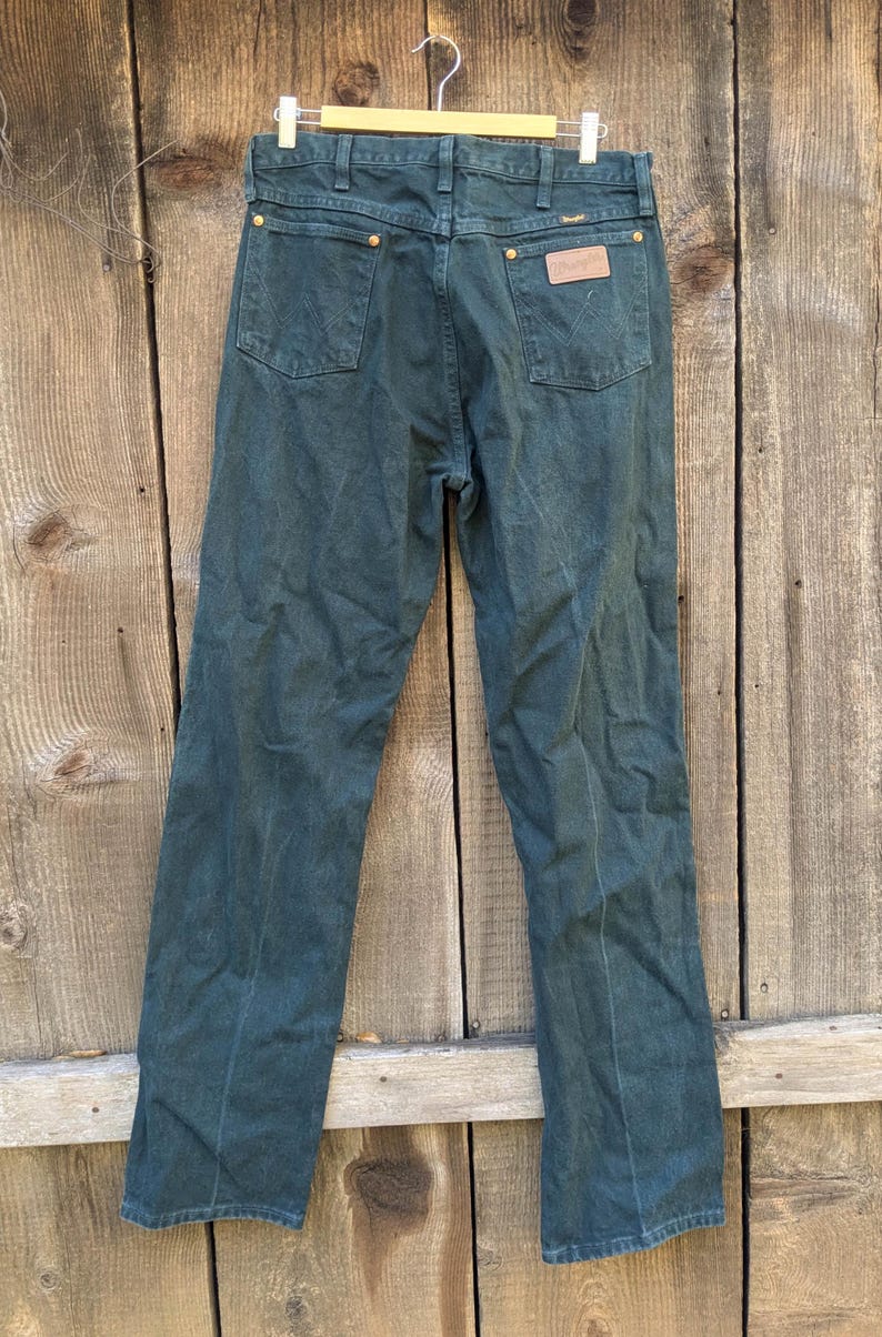 May include: A pair of dark green denim jeans with a leather patch on the back pocket that says "Wrangler".