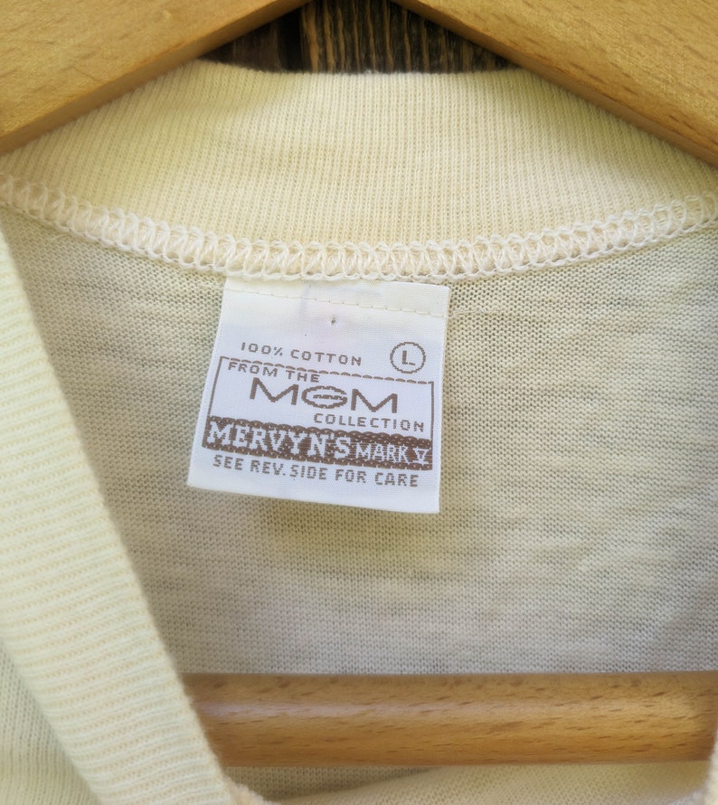 May include: A white 100% cotton t-shirt tag with the text "From the MOM Collection Mervyn's Mark V See Rev. Side for Care" and a size L label.