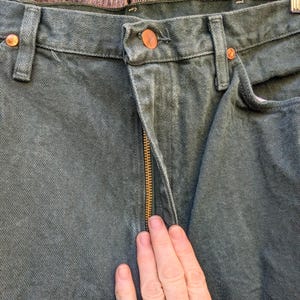 May include: A pair of dark green denim jeans with a gold zip. The jeans have a classic five-pocket style and a straight leg.