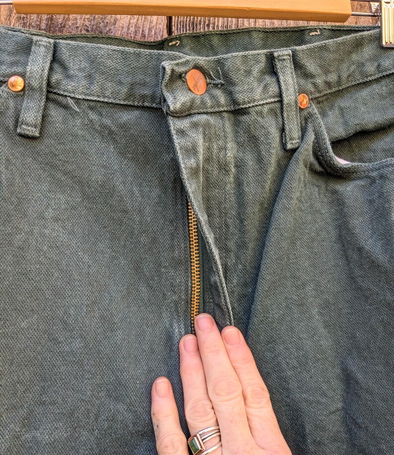 May include: A pair of dark green denim jeans with a gold zip. The jeans have a classic five-pocket style and a straight leg.