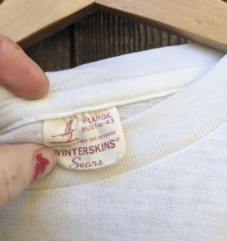 May include: White t-shirt with a red tag that says "X-Large Bust 41-43" and "Winterskins Sears" with a skier graphic.