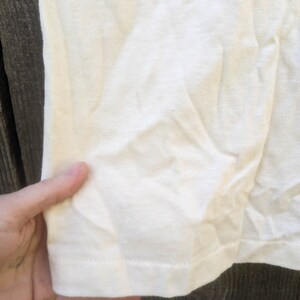 May include: Close-up of the bottom hem of a white t-shirt. The fabric is a soft, knit material.
