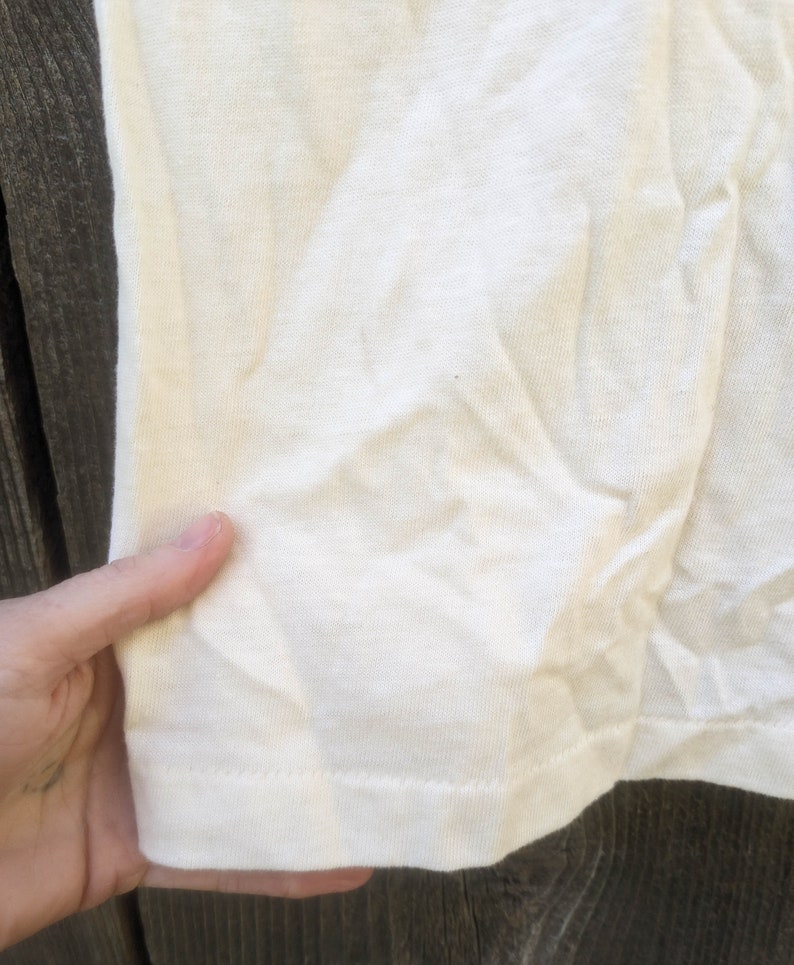 May include: Close-up of the bottom hem of a white t-shirt. The fabric is a soft, knit material.