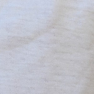 May include: Close-up of a white knitted fabric with a subtle texture. The fabric is smooth and soft, with a slightly grainy appearance.