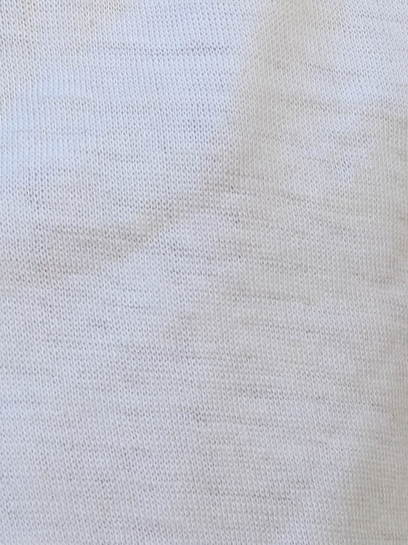 May include: Close-up of a white knitted fabric with a subtle texture. The fabric is smooth and soft, with a slightly grainy appearance.