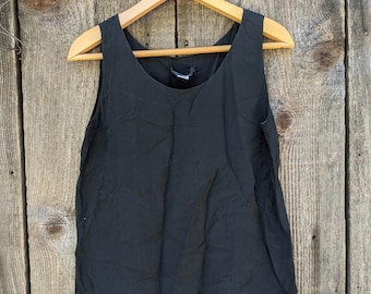 May include: A black sleeveless top hanging on a wooden hanger against a woodgrain background.