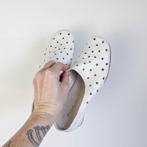 May include: A pair of white leather slip-on shoes with star-shaped cutouts. The shoes have a rounded toe and a low heel. The brand name "Beauty fis" is visible on the inner sole.
