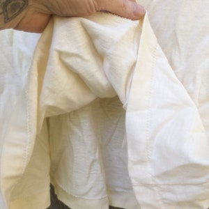 May include: Close-up of the inside of a white t-shirt, showing the stitching and fabric texture.