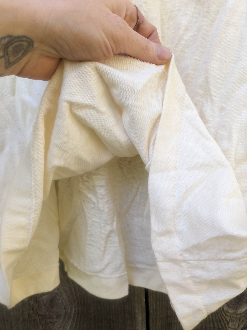May include: Close-up of the inside of a white t-shirt, showing the stitching and fabric texture.