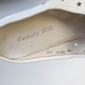 May include: Close-up of a white shoe interior with the text "Beauty fish" printed in gray. The shoe has star-shaped cutouts and the numbers "9015 230" are visible.