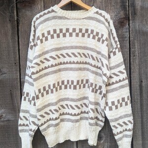 May include: A cream-colored sweater with a brown geometric pattern. The sweater has a crew neck and long sleeves.