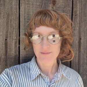 May include: A person with red hair wearing round glasses and a striped button-down shirt.
