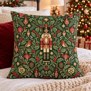 May include: A square throw pillow featuring a dark green background with a repeating pattern of red berries, pine cones, gold stars, and ornaments. A central nutcracker figure stands flanked by two small brown birds with red chests.