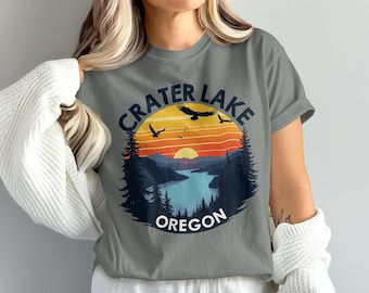 May include: Gray t-shirt with a vintage-style graphic of Crater Lake, Oregon. The graphic features a sunset over a lake with mountains and trees, and a flying eagle.