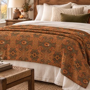May include: A woven throw blanket featuring a repeating pattern of sleeping foxes curled within circular floral frames. The design incorporates deep orange, rust, and muted green tones, creating a dense, intricate botanical motif across the fabric.