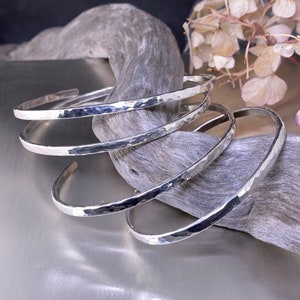 Peut inclure: Quatre bracelets en argent martelés empilés sur un morceau de bois flotté.
