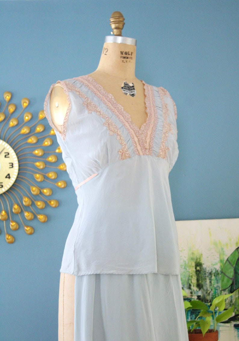 K&ouml;nnte beinhalten: Ein hellblaues, &auml;rmelloses Schlupfkleid mit einem rosa Spitzenbesatz am Ausschnitt. Das Kleid befindet sich auf einer wei&szlig;en Kleiderpuppe.