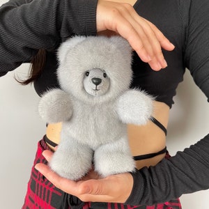 Könnte beinhalten: Ein kuscheliger, grauer Teddybär mit einer flauschigen, fellartigen Textur. Der Bär hat eine kleine, schwarze Nase und Knopfaugen. Ein klassisches Spielzeug, perfekt für Kinder oder Sammler.