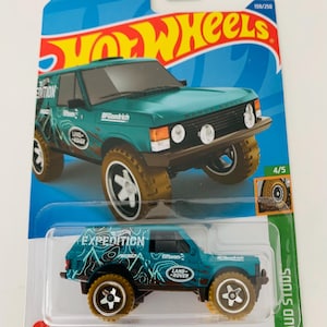 May include: A teal Hot Wheels Range Rover Classic toy car with brown mud-effect tires. The packaging includes the text "GUARANTEED FOR LIFE" and "MUD STUDS". The car has "EXPEDITION" and "LAND ROVER" graphics.