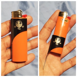 May include: Two orange lighters with black and silver accents. One lighter has a black and silver design with a graphic of a person and leaves. The other lighter has a black and silver design with the word "BIC" printed on it.