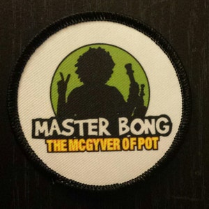 Peut inclure: Un &eacute;cusson rond blanc avec des coutures noires autour des bords. L'&eacute;cusson pr&eacute;sente un cercle vert avec une silhouette noire d'une personne tenant un bang. Le texte "MASTER BONG THE MCGYVER OF POT" est imprim&eacute; en lettres jaunes et noires.