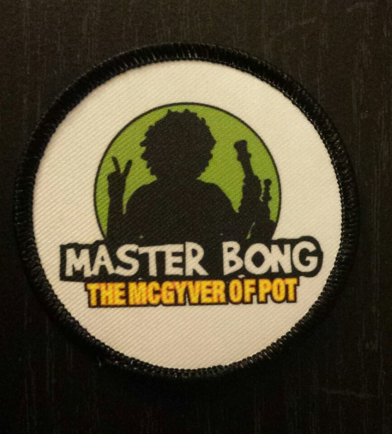 Peut inclure: Un &eacute;cusson rond blanc avec des coutures noires autour des bords. L'&eacute;cusson pr&eacute;sente un cercle vert avec une silhouette noire d'une personne tenant un bang. Le texte "MASTER BONG THE MCGYVER OF POT" est imprim&eacute; en lettres jaunes et noires.